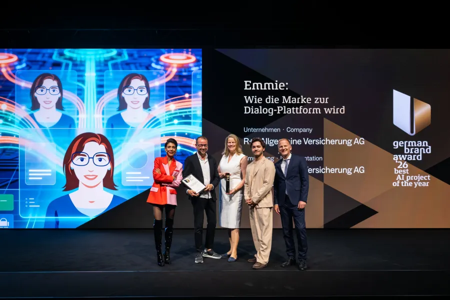 Sven Schmitt, Anke Josten und Eldin Thomas von der R+V Versicherung nehmen die Best-of-Best-Auszeichnung des German Brand Award 2026 für den KI-Chatbot Emmie entgegen, umrahmt von den Juroren Sophia Rödiger (links) und Christian Rummel (rechts).