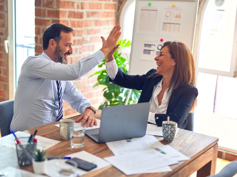 Zwei Personen in einem Büro lächeln und geben sich gegenseitig ein High-Five.