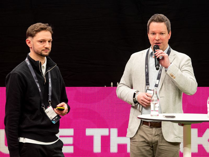 Auf dem Bild stehen unser CEO Ulf Loetschert und Merlin Klüver vom 1. FC Köln gemeinsam auf einer Bühne der SPOBIS 2026 vor einer leuchtend pinkfarbenen Videowand.